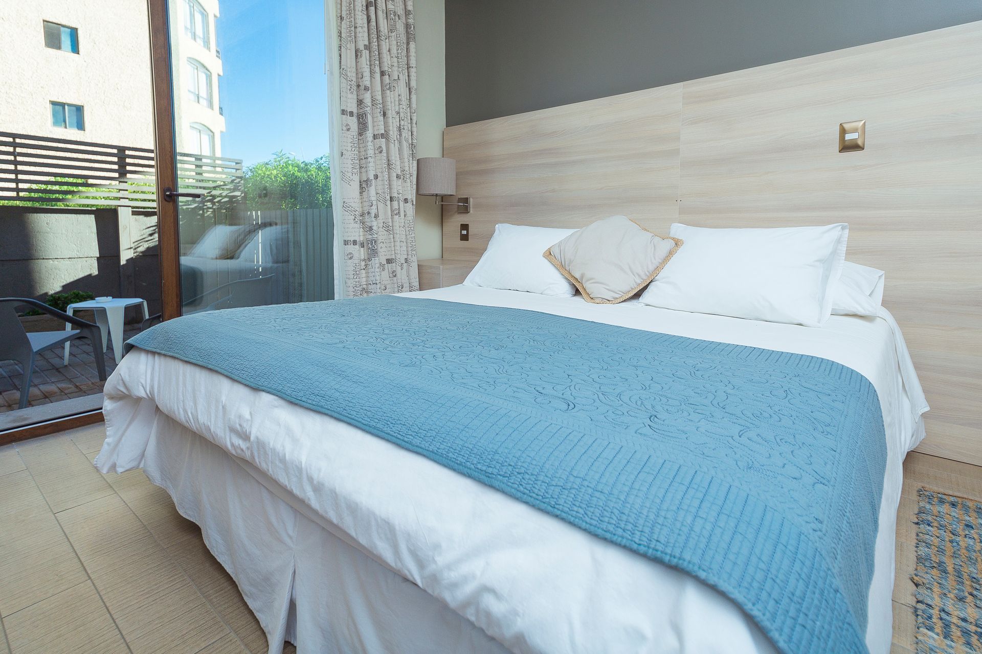 A bed with white sheets and a blue blanket in a hotel room.
