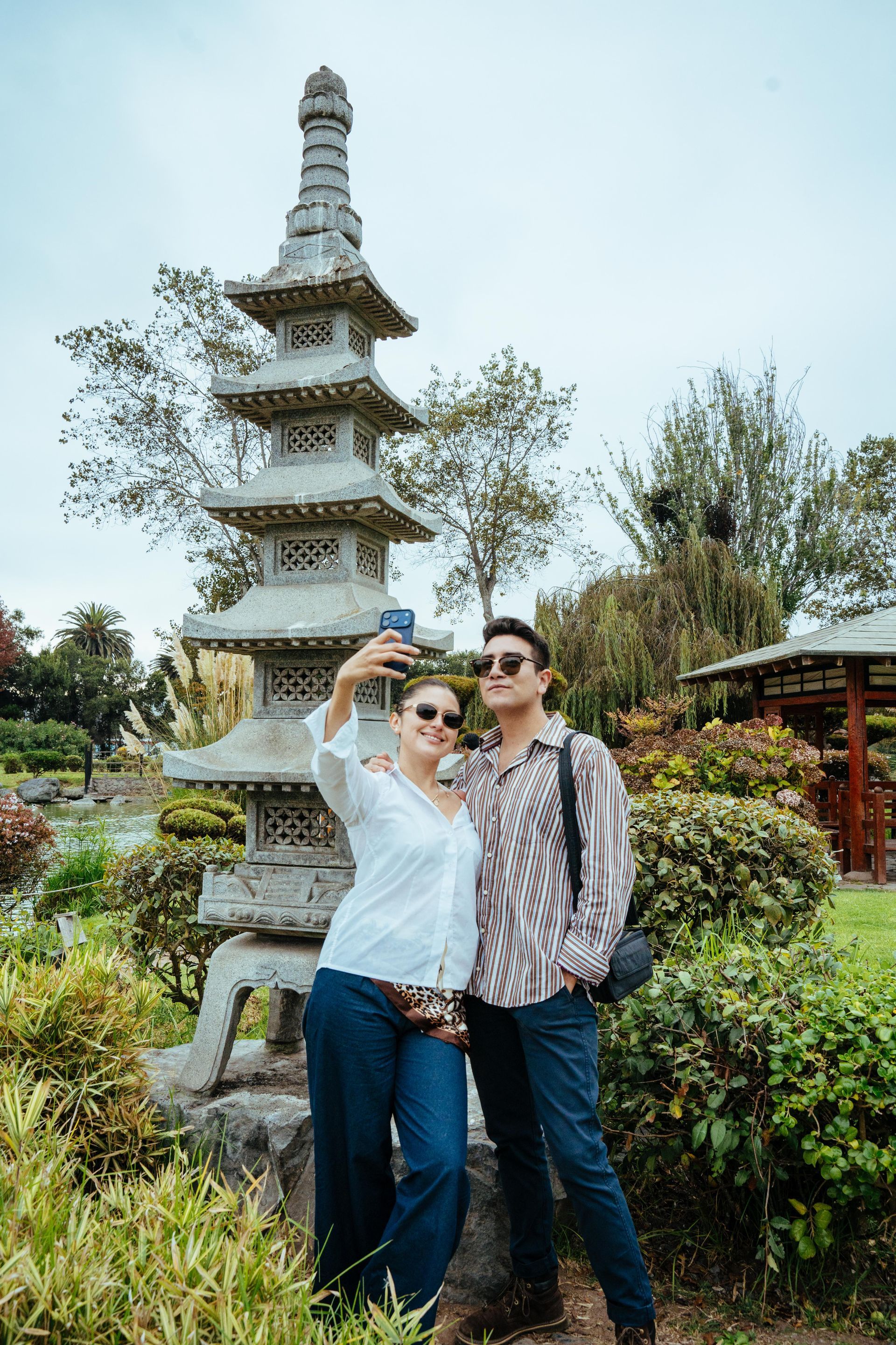 Couple standing on a red arched bridge in a green garden with trees and shrubs