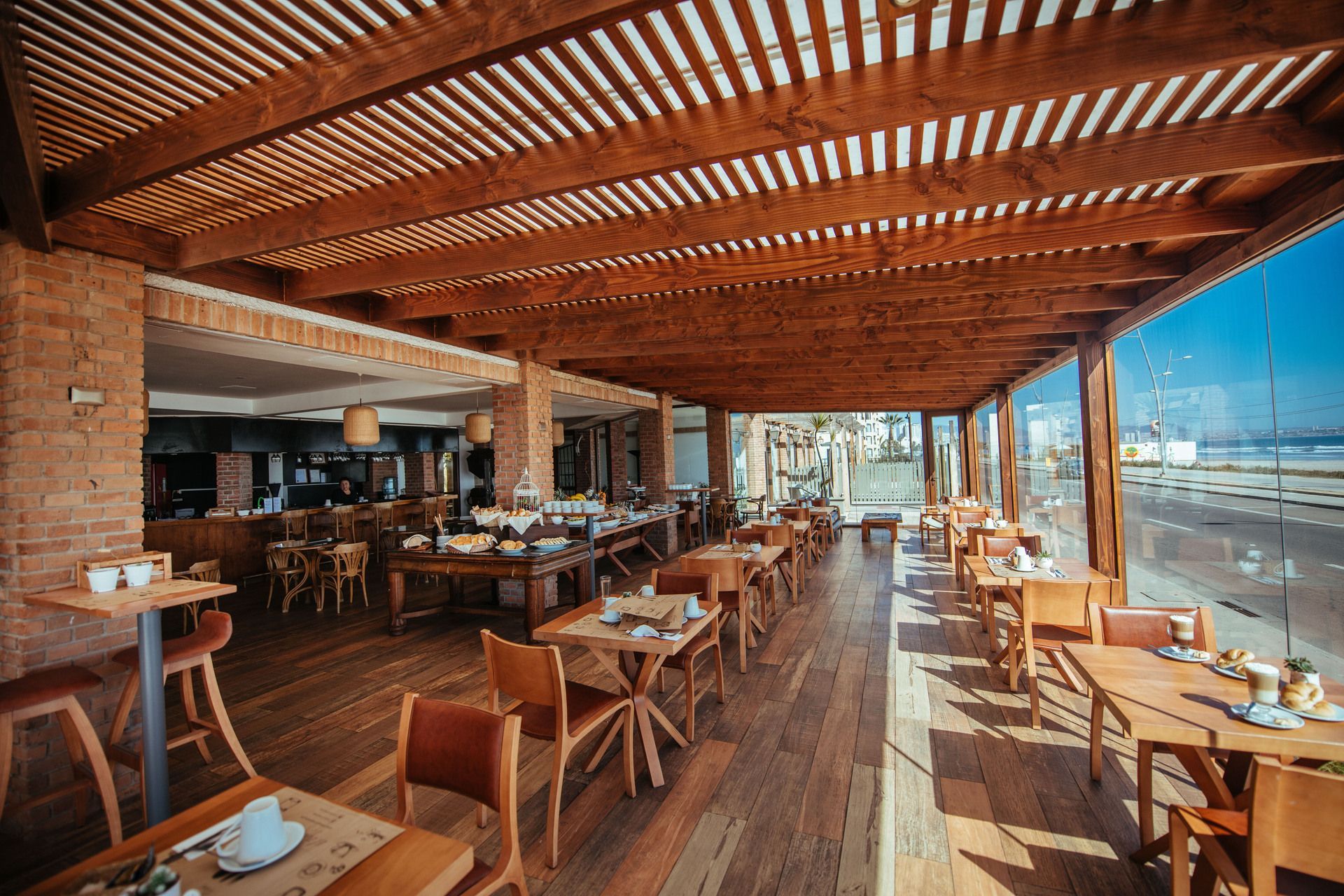 A restaurant with tables and chairs under a wooden roof.