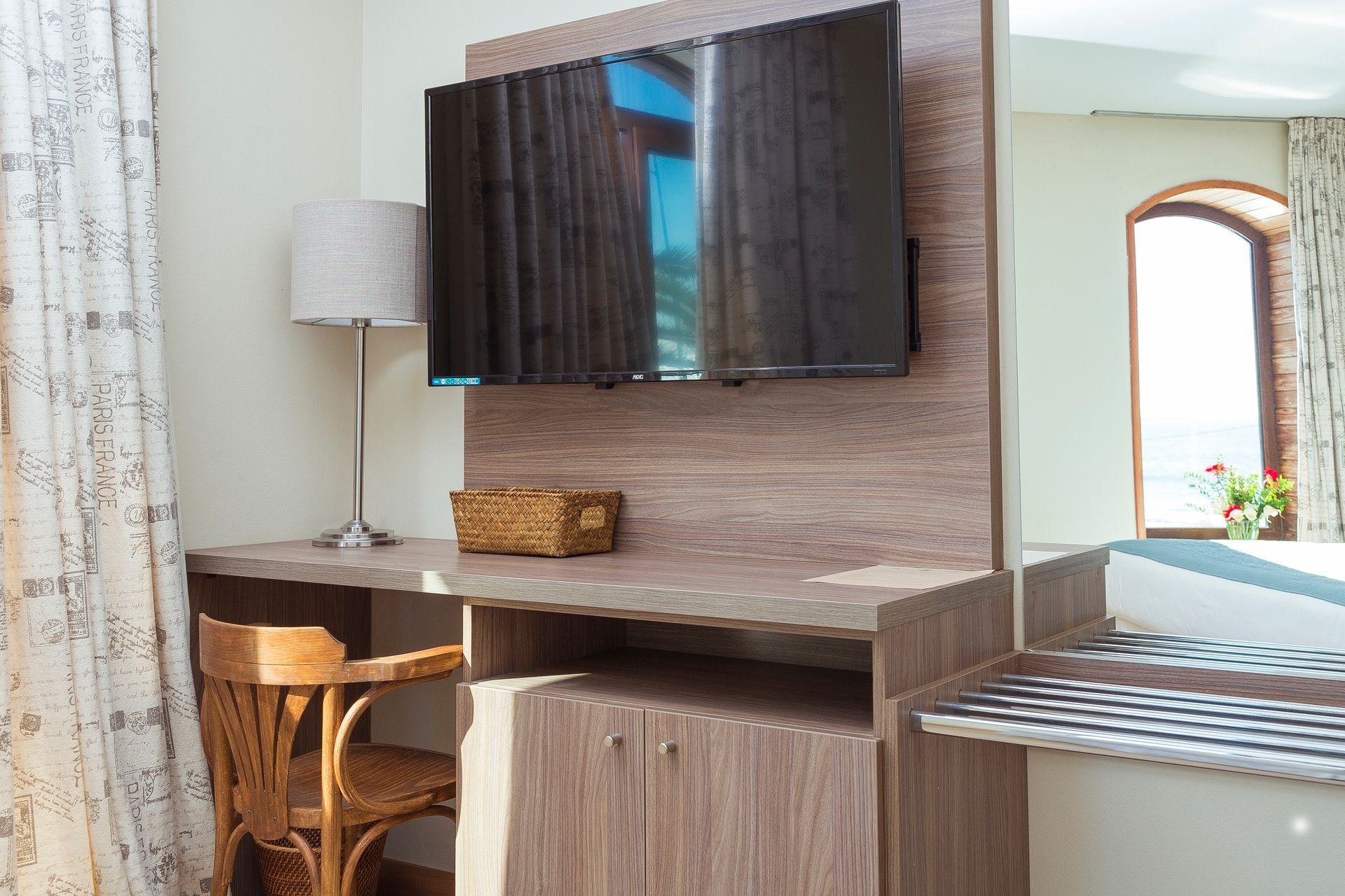 A hotel room with a desk , chair , lamp and television.