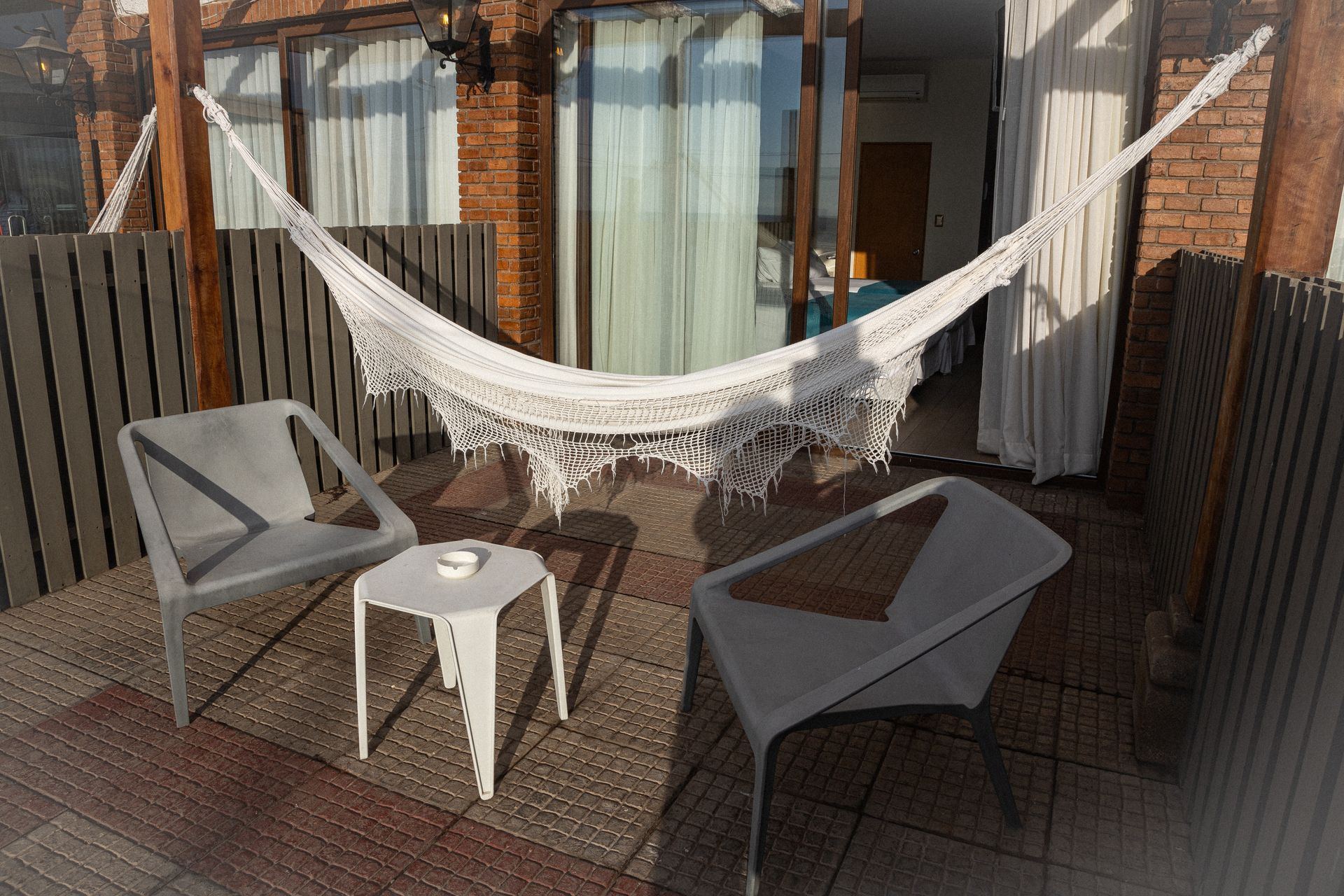 A hammock is hanging over a patio with chairs and a table.