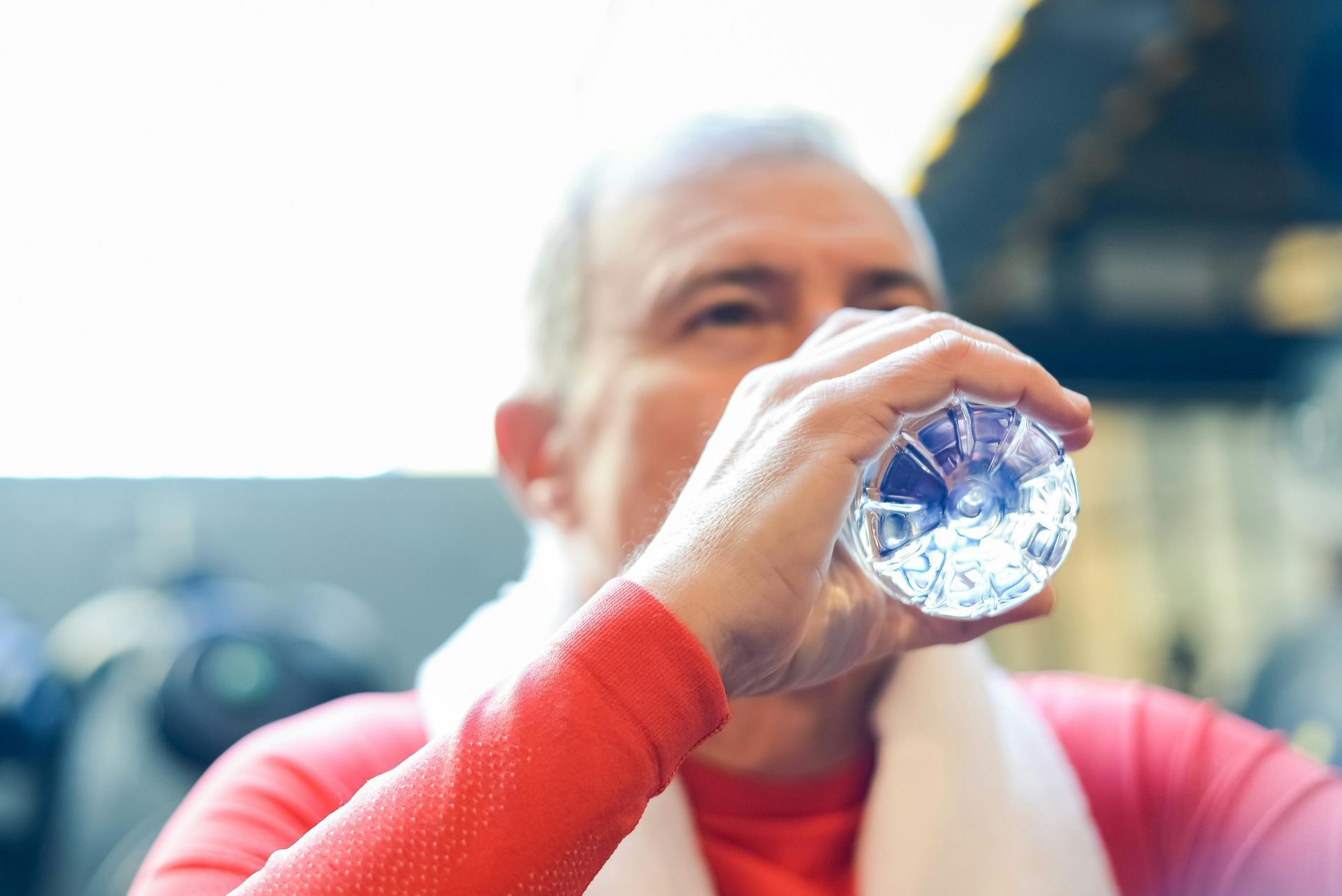 Person in red drinks water from a clear bottle, with a blurred stadium background
