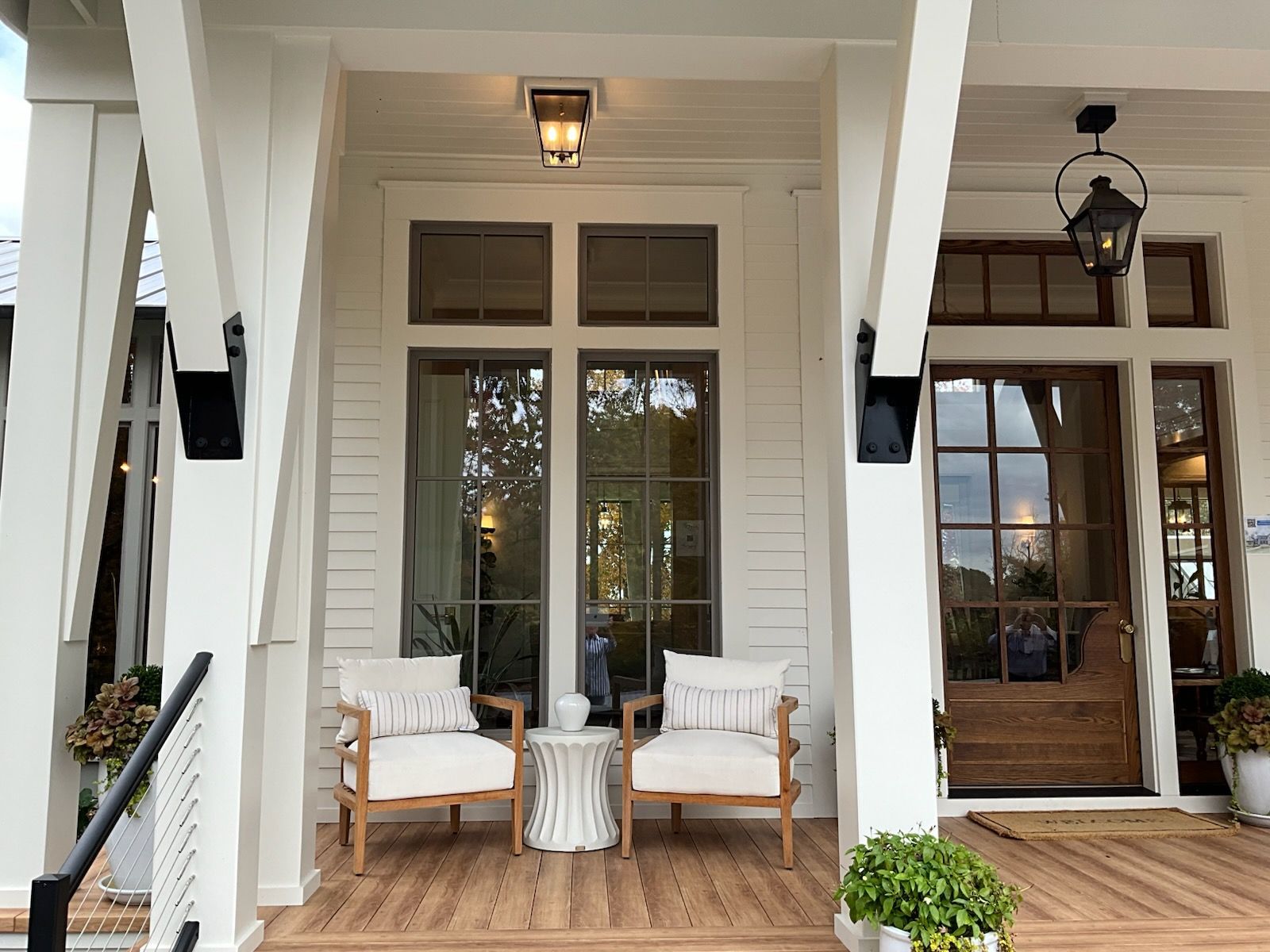 White porch with wooden chairs, glass windows, and a brown front door.