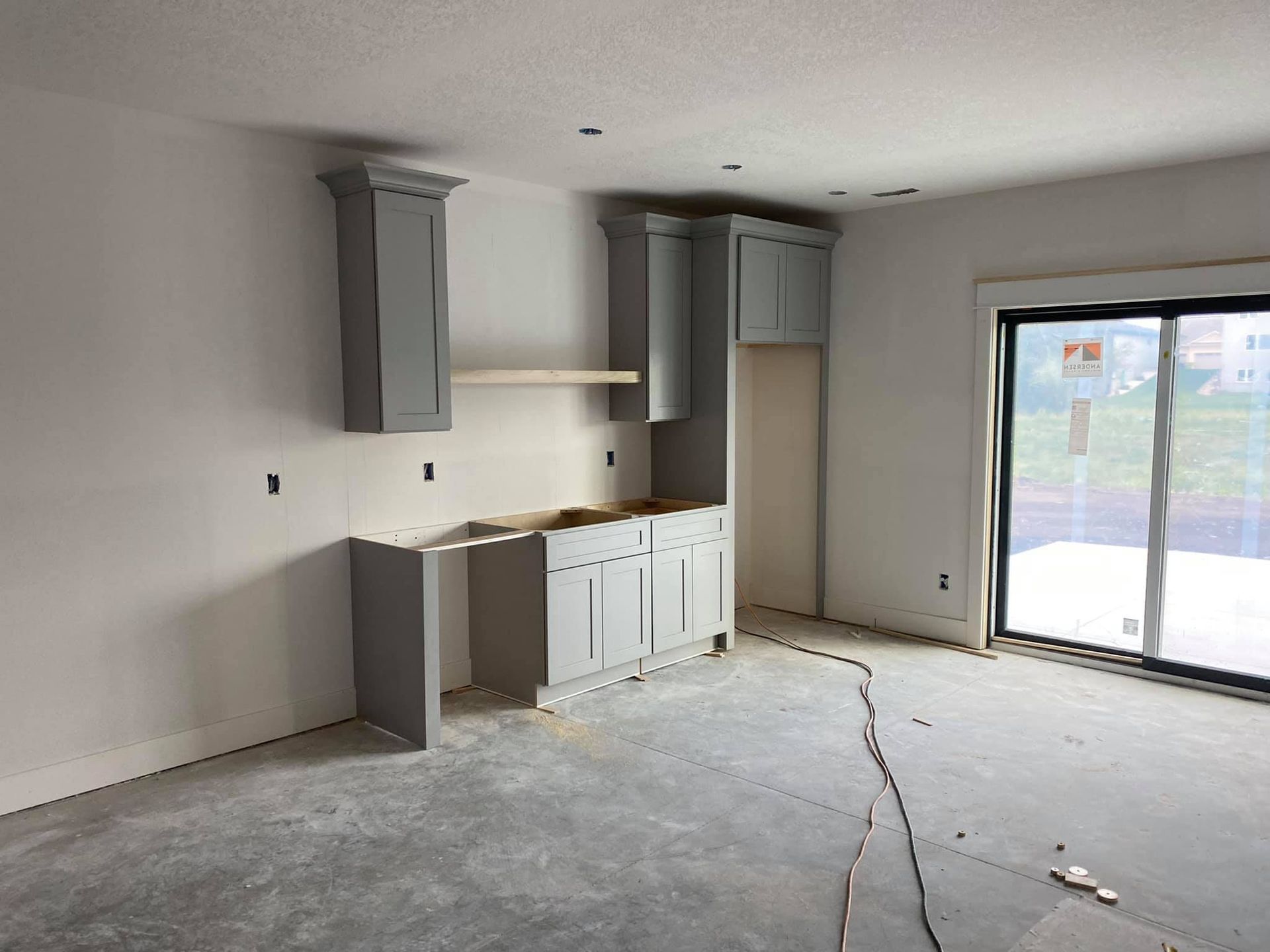 An empty room with a sliding glass door and gray cabinets.