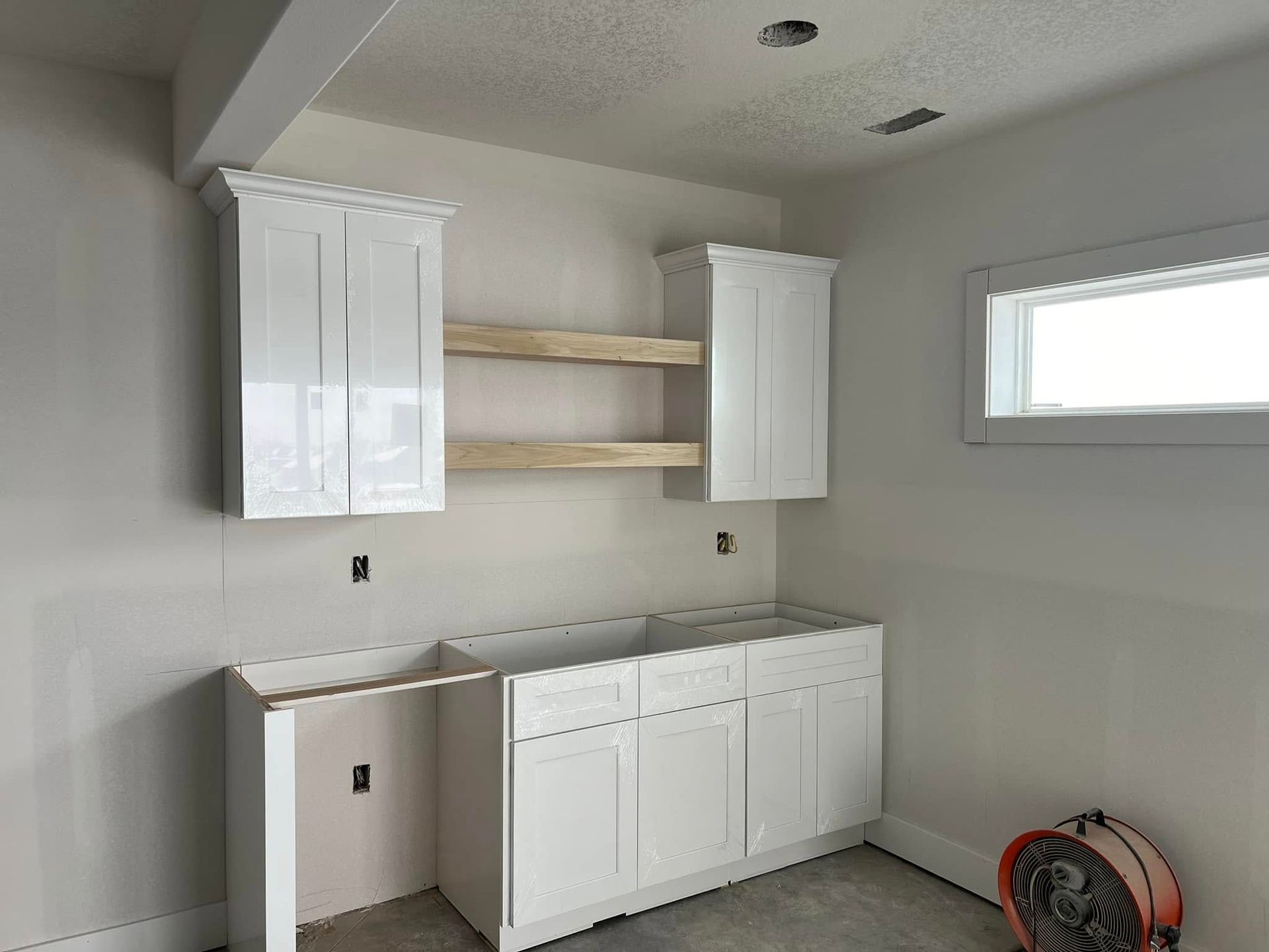 A kitchen under construction with white cabinets and wooden shelves.