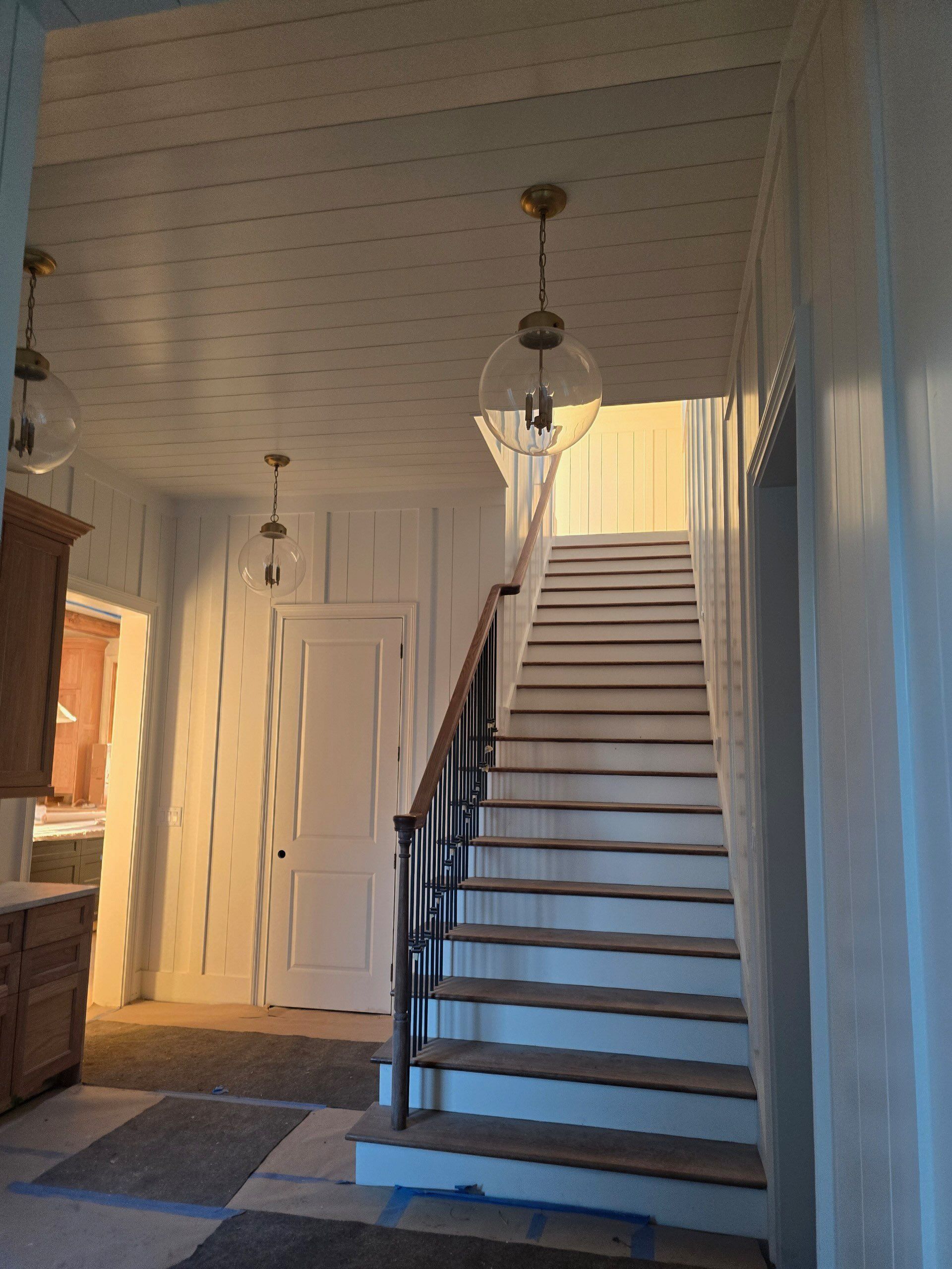 Stairwell with white paneled walls and ceiling, wooden stairs, and globe pendant lights.