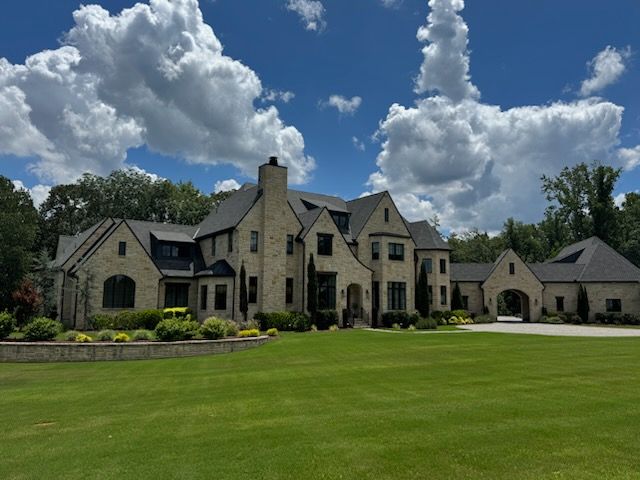 Large stone house with a manicured lawn under a blue sky with fluffy white clouds.