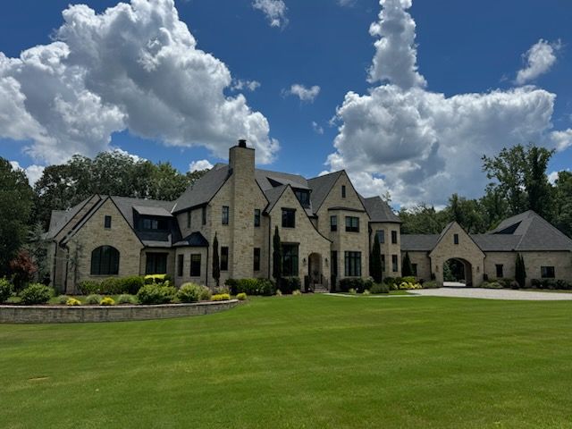 Large stone house with manicured lawn and bright blue sky dotted with puffy clouds.