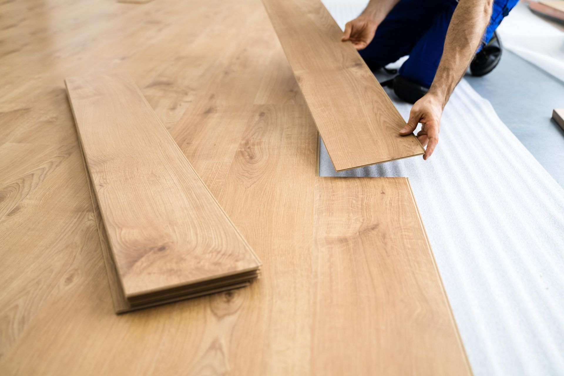 Person installing wood flooring, with planks on underlayment.