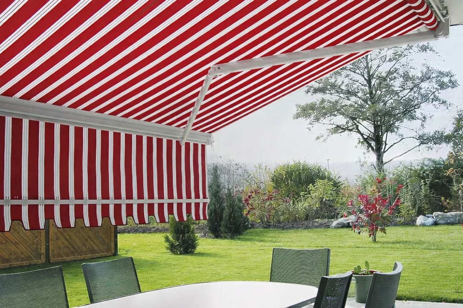 Tenda da sole a strisce rosse e bianche sopra una zona pranzo all'aperto su un prato erboso.