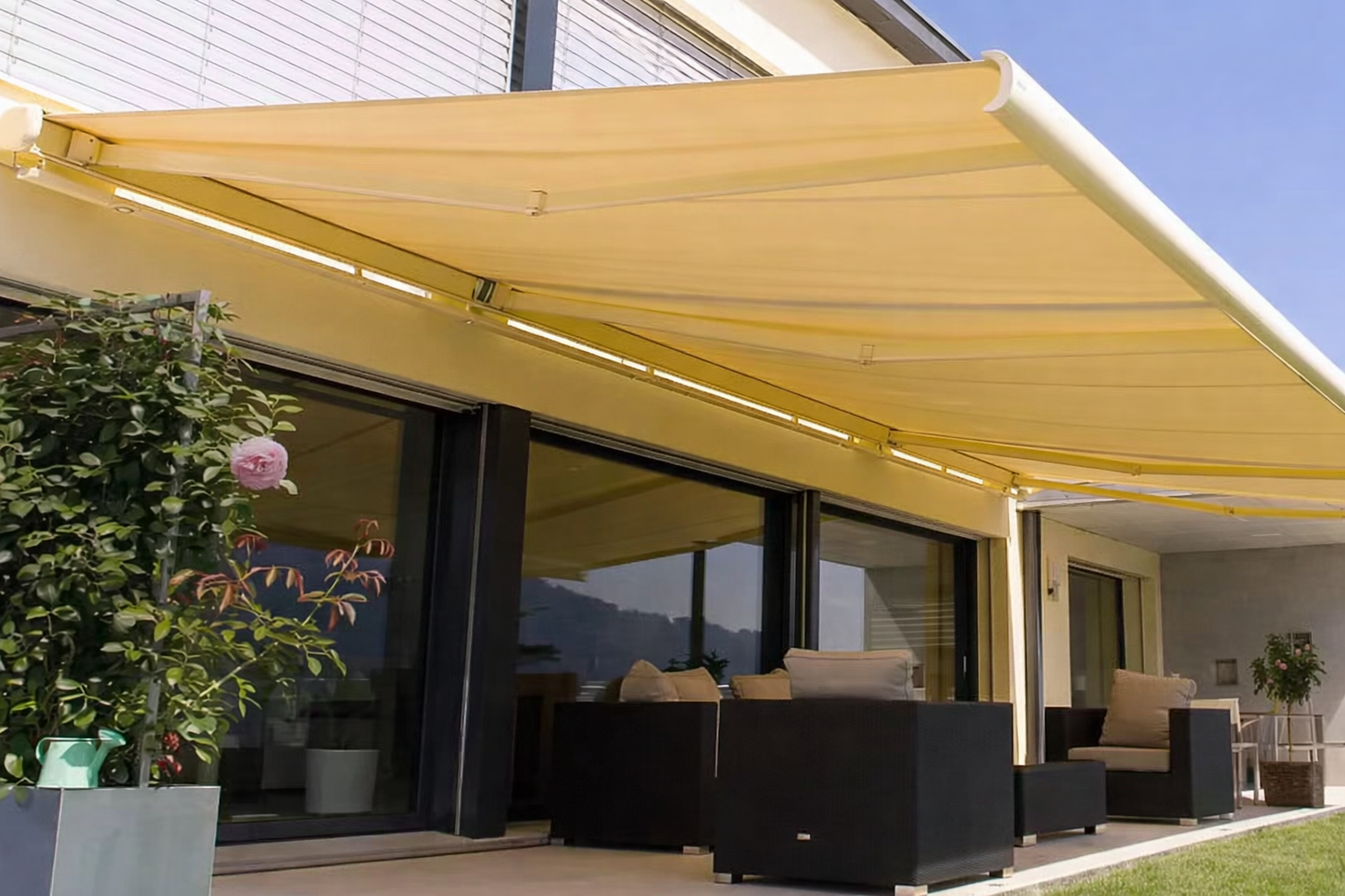 Tenda da sole gialla che ombreggia un patio con posti a sedere; si vede la vista sulle montagne.