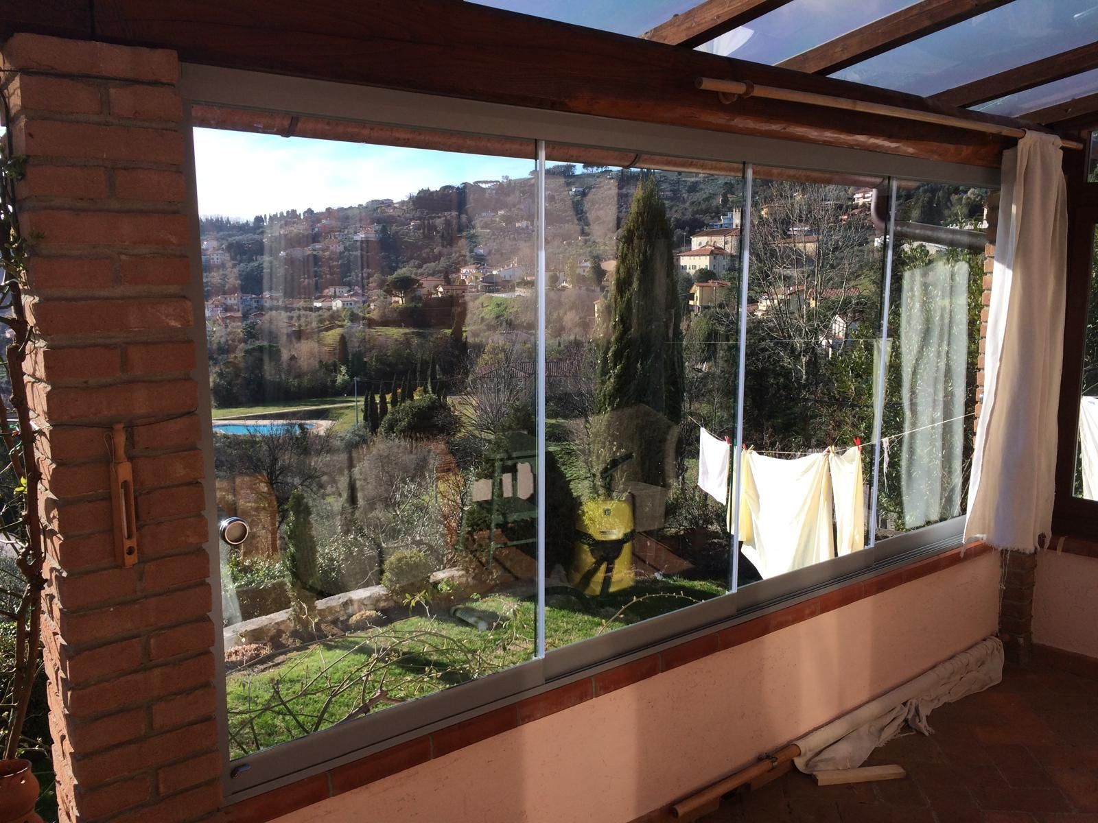 Veranda con vetrate e vista sul giardino e sulla collina, illuminata dalla luce del sole.