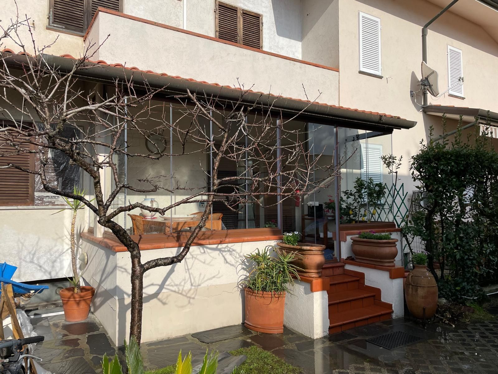 Un edificio a due piani con un portico in vetro, gradini e un albero spoglio nel cortile anteriore.