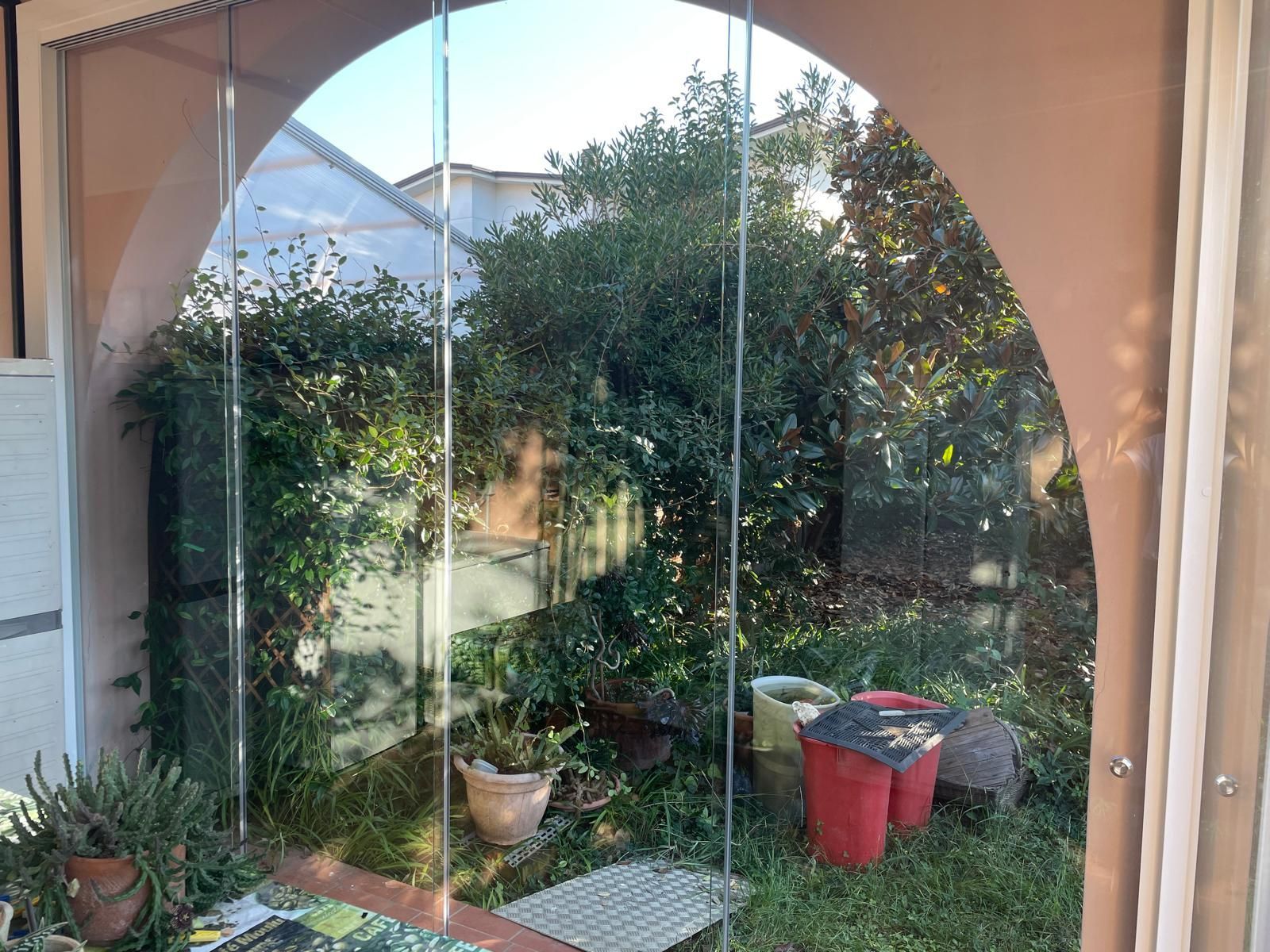 Vista attraverso un recinto ad arco trasparente su un giardino soleggiato con vegetazione lussureggiante