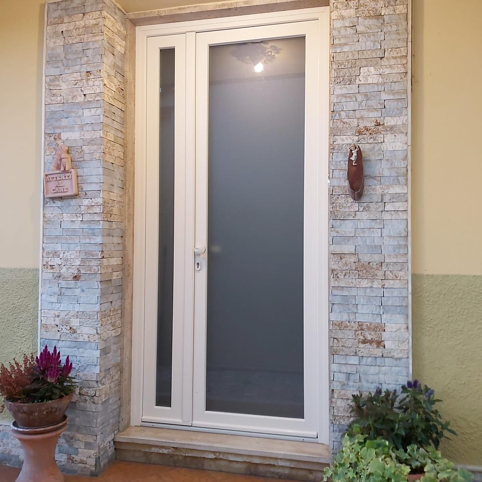 Doppie porte bianche con pannelli in vetro incorniciati da colonne in pietra; piante in vaso fiancheggiano l'ingresso.