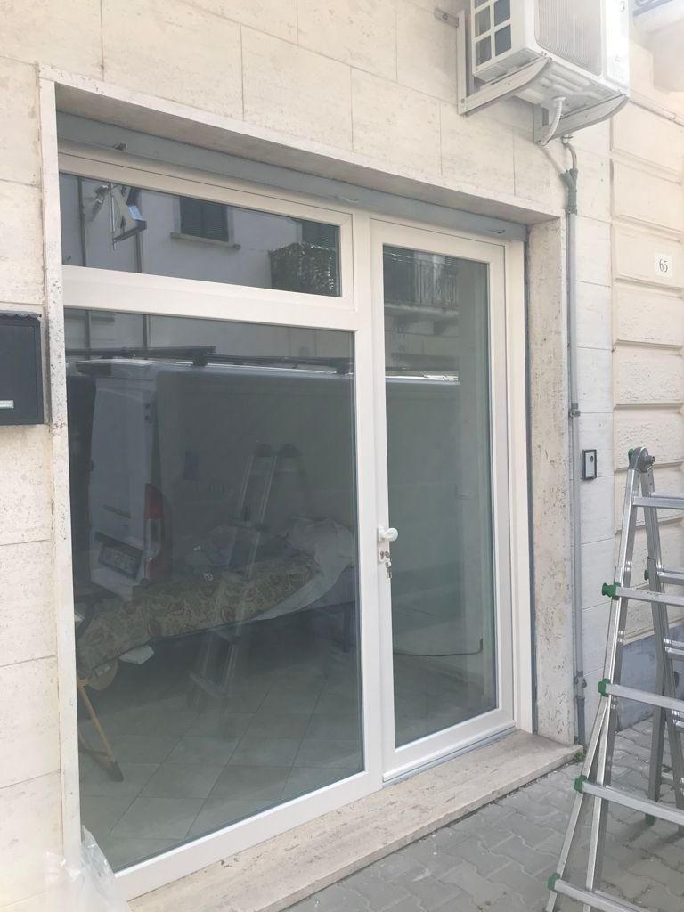 Porta e finestra in vetro con cornice bianca. Esterno dell'edificio beige. Una scala appoggiata al muro.