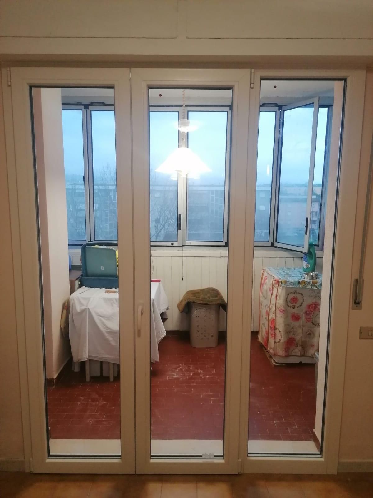 Porta a vetri a tre ante che conduce a un balcone con tavoli e finestre. Il pavimento è rosso.