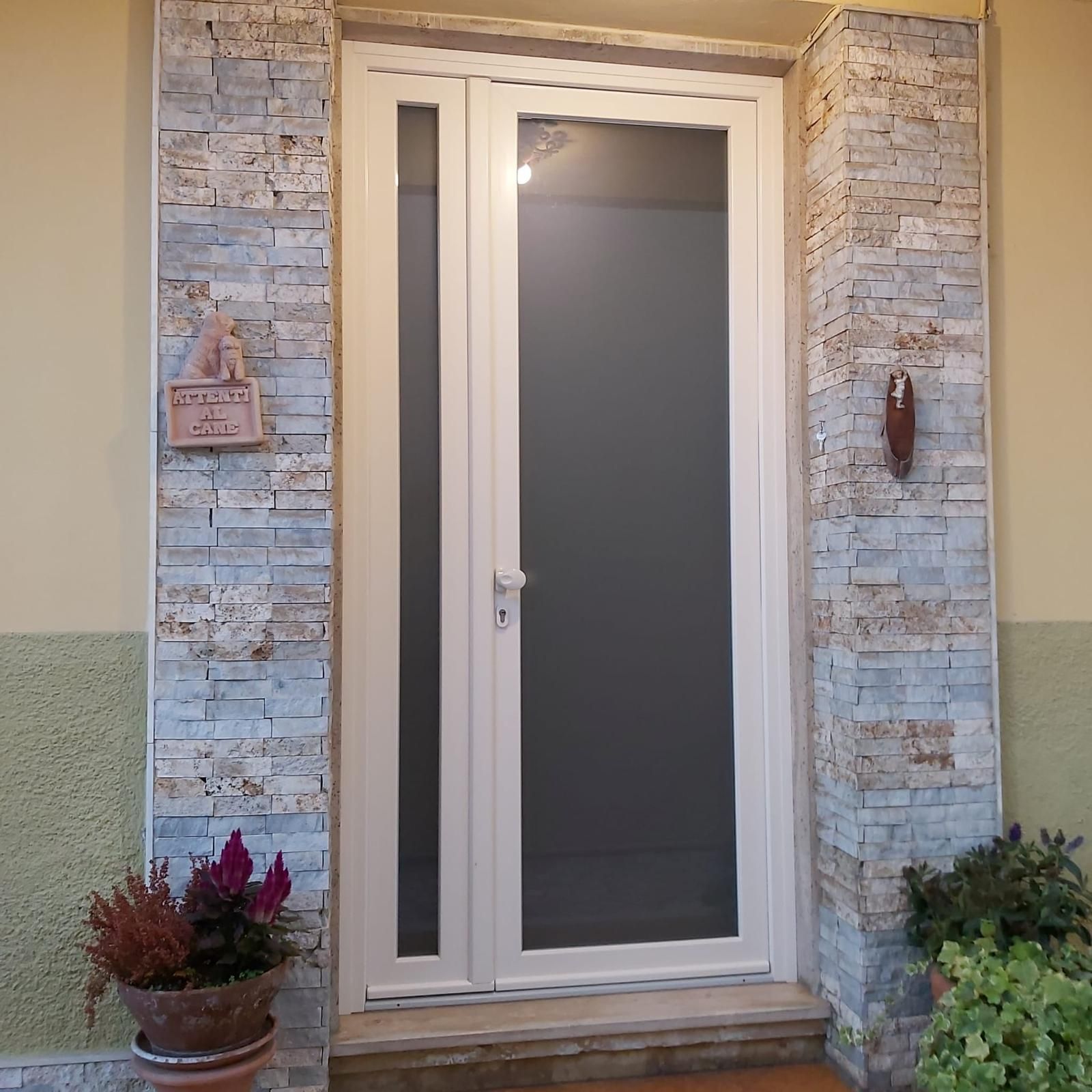 Porta bianca con luce laterale, circondata da pietra. Nelle vicinanze ci sono piante in vaso marroni.