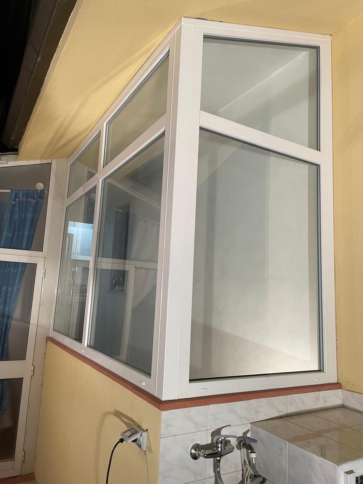 Finestre con cornice bianca su una parete gialla, angolo obliquo. Apparecchi idraulici sul bancone sottostante.