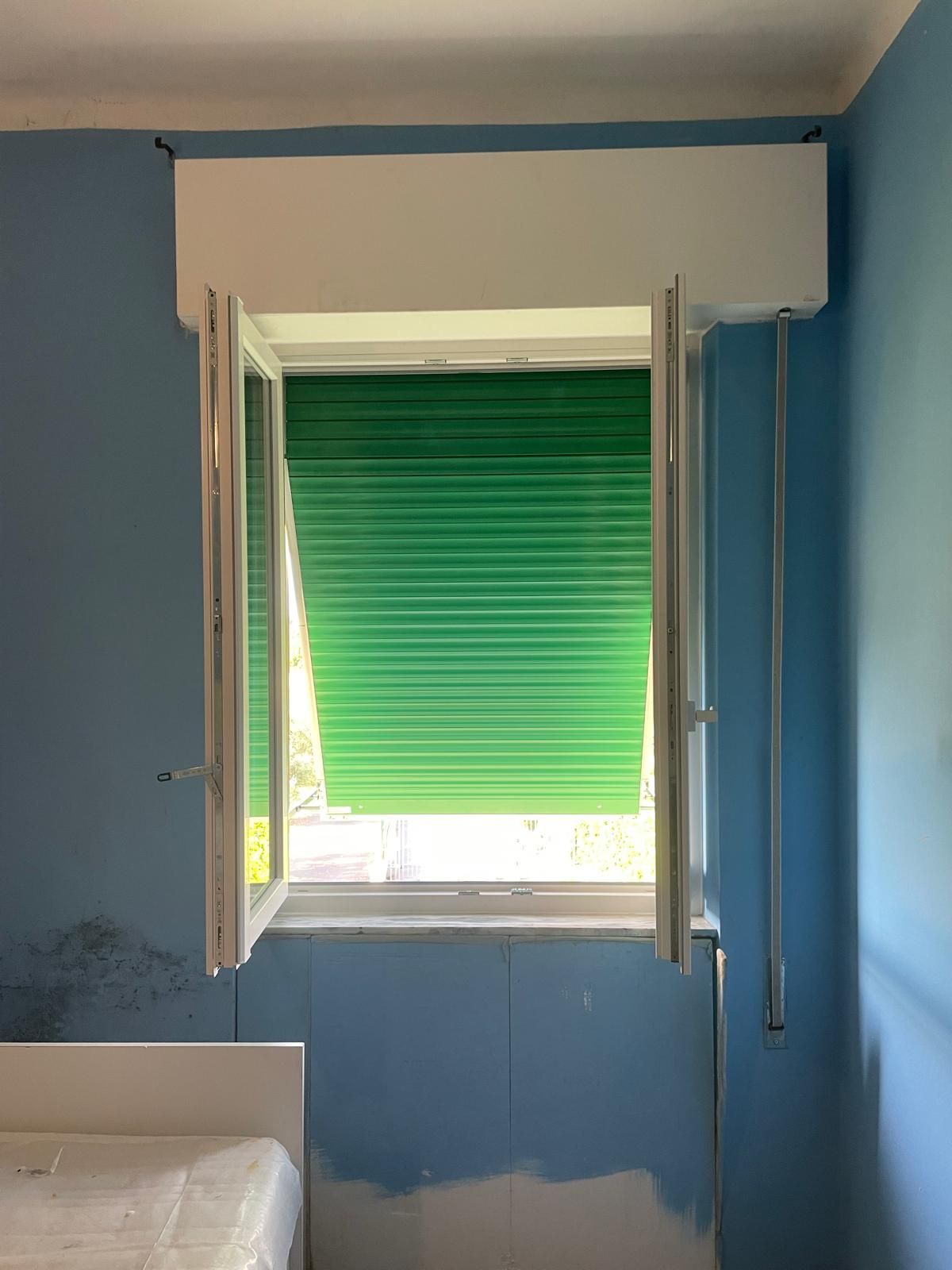 Finestra con cornici bianche aperte, persiane verdi e parete blu.