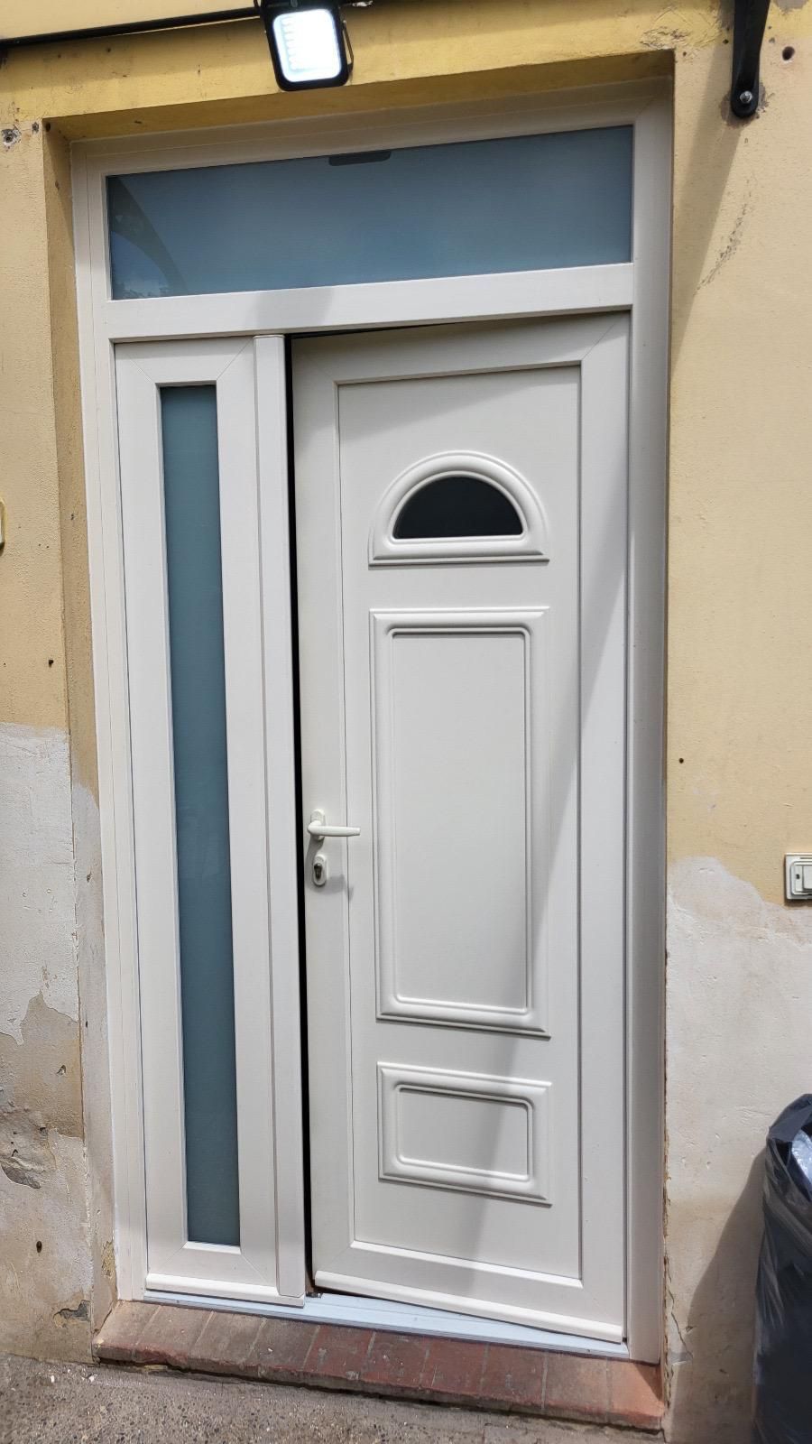 Porta bianca con pannello di vetro, sotto una traversa blu, in un edificio giallo chiaro.
