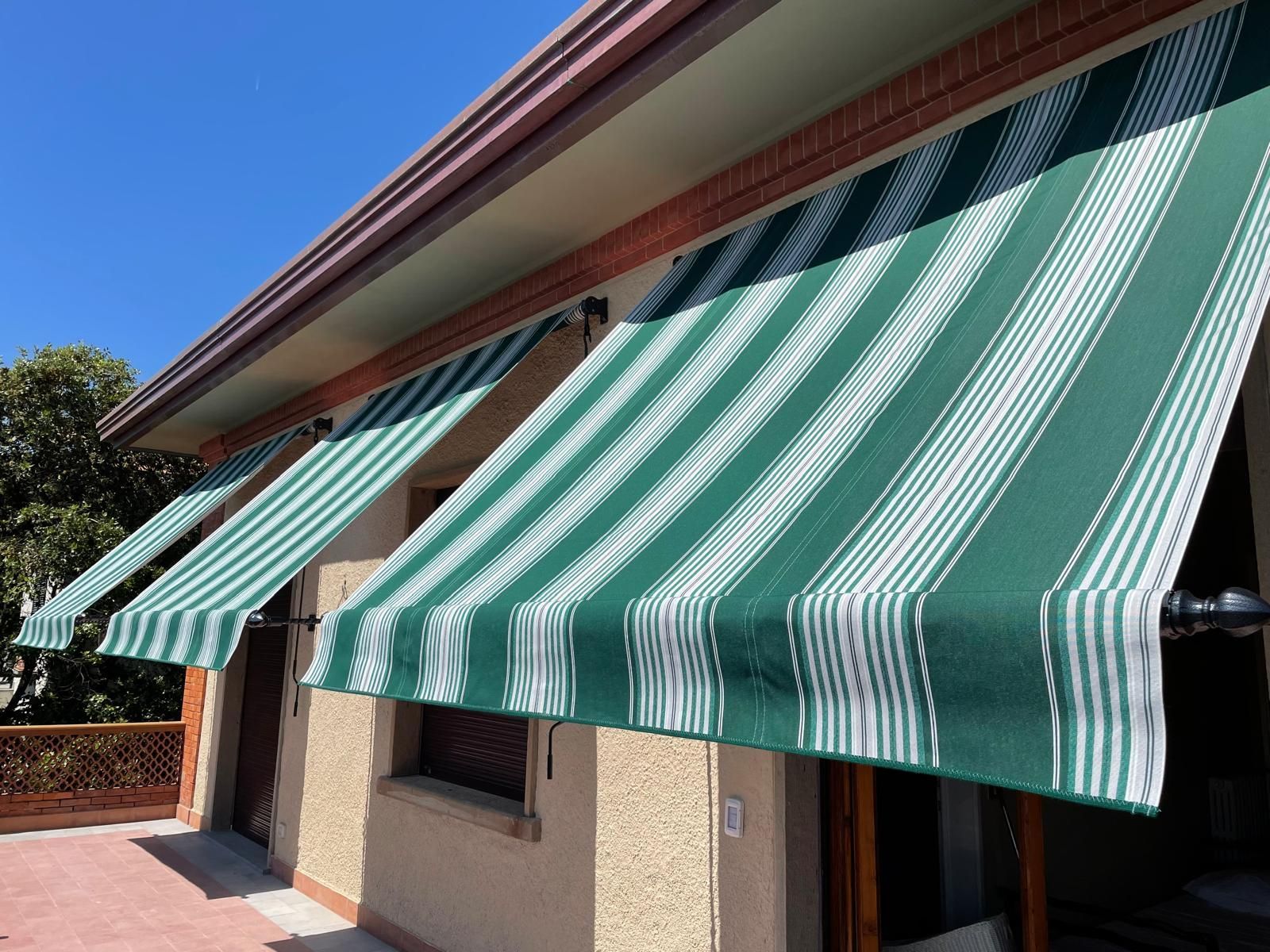 Nelle giornate di sole, le tende a strisce verdi e bianche ombreggiano le finestre di un edificio.