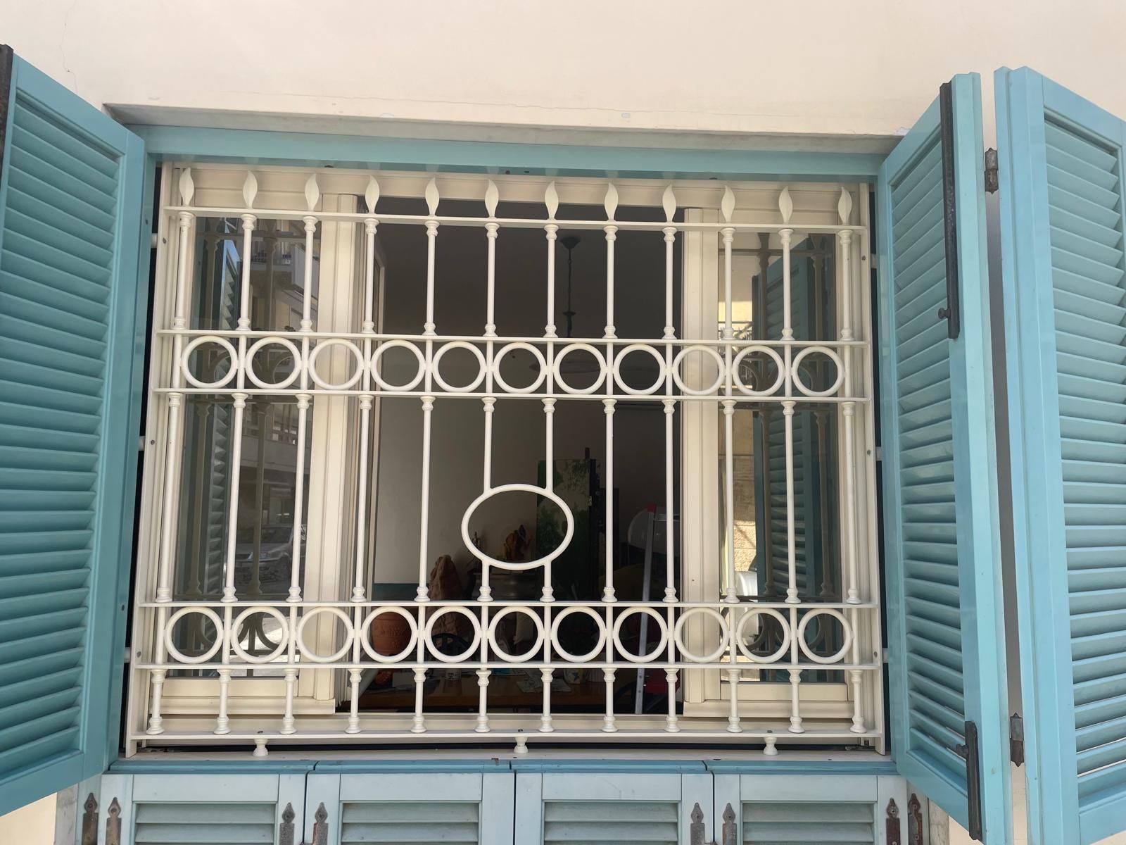 Finestra con persiane blu e inferriate di sicurezza in ferro bianco.