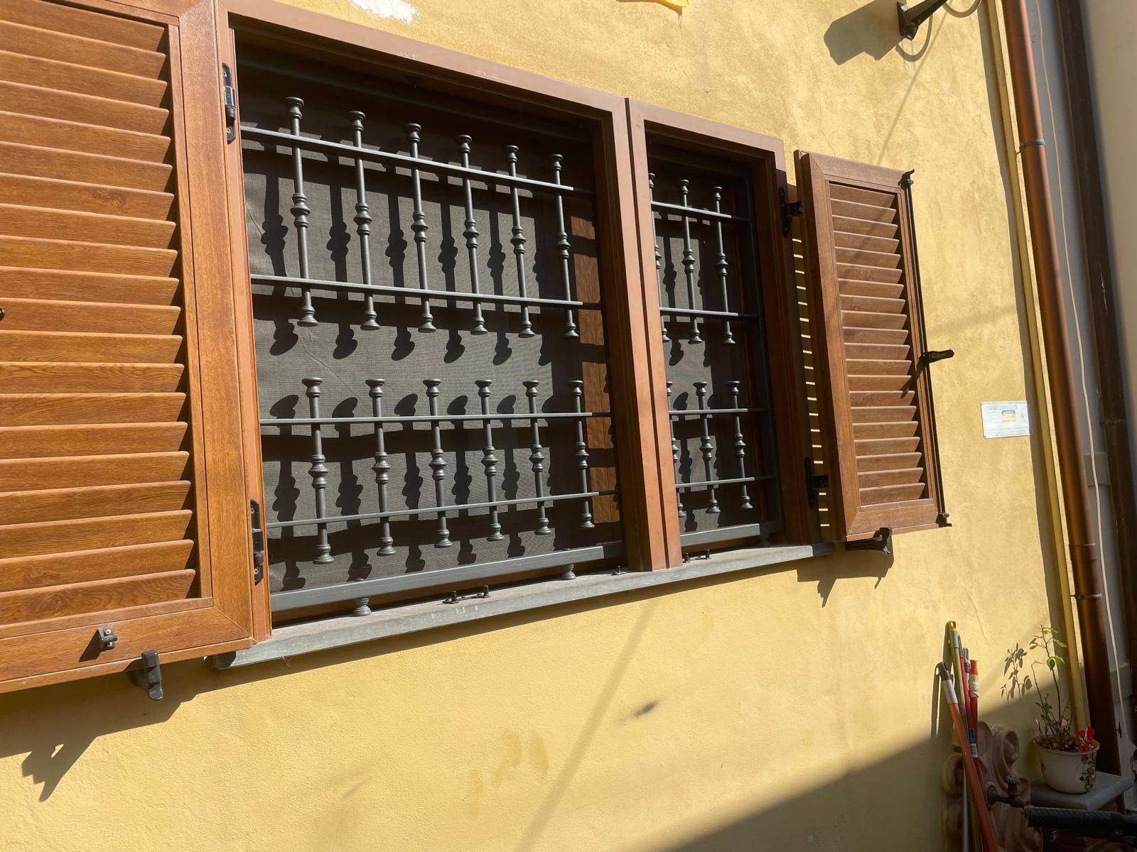 Persiane marroni e sbarre di sicurezza su un edificio giallo.