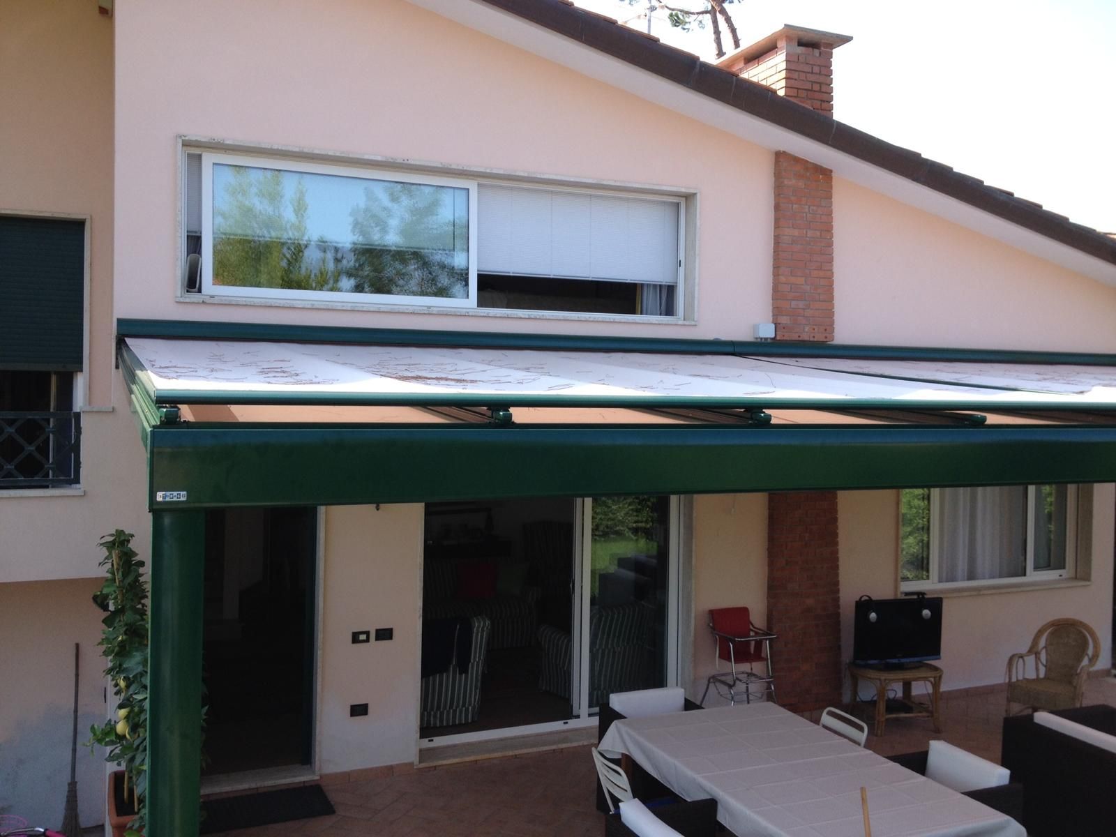 Casa beige con una tenda da sole verde sopra il patio. Sono visibili porte scorrevoli in vetro e una finestra.