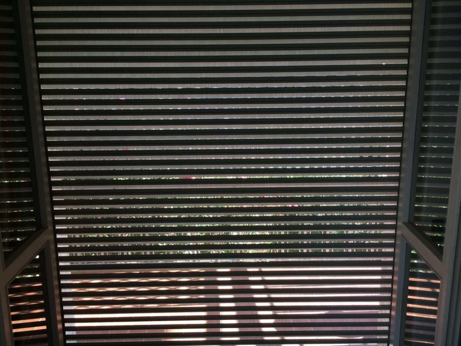 Vista dall'alto di un soffitto a doghe che lascia filtrare la luce naturale, proiettando ombre sottostanti.