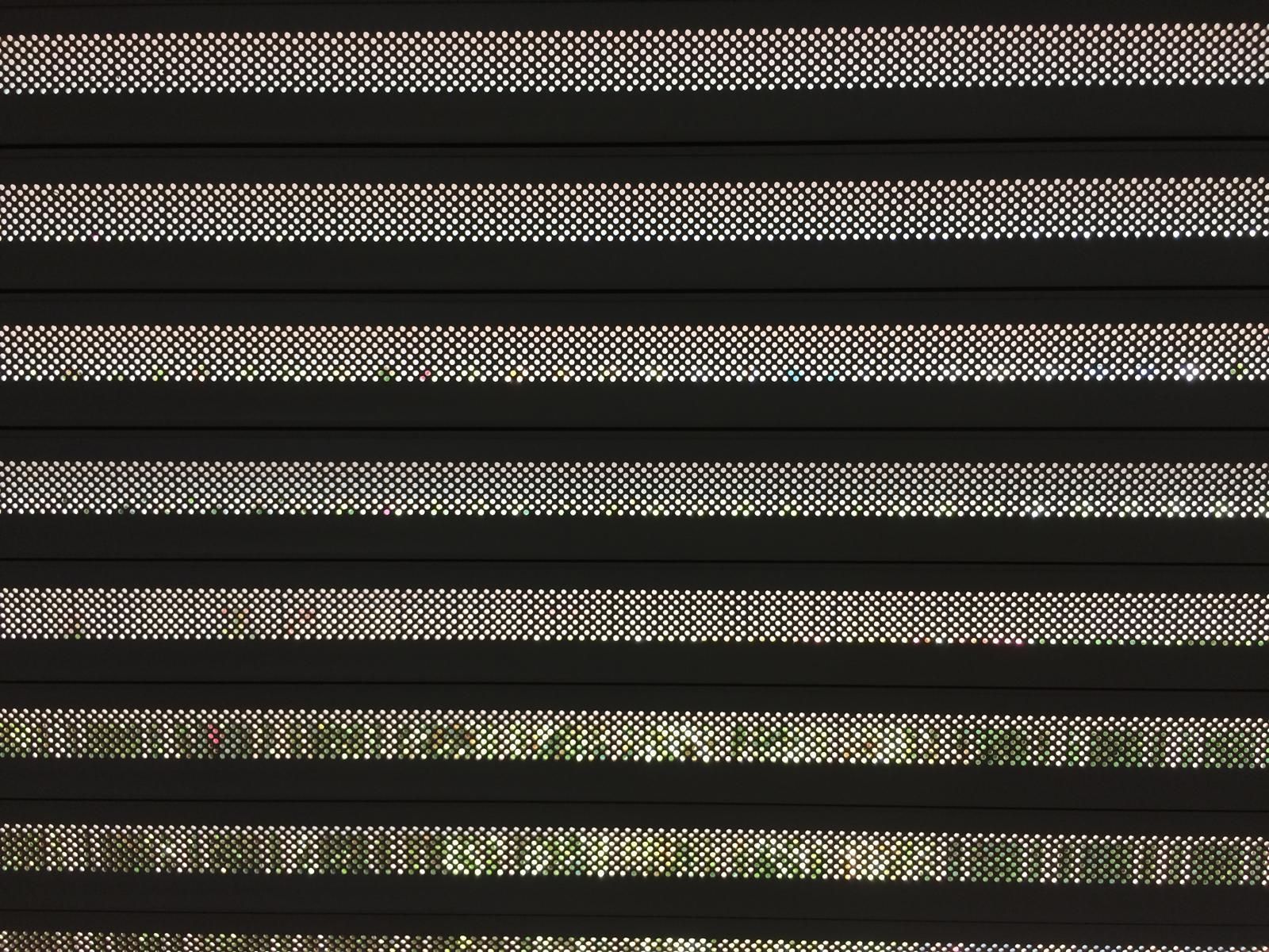 Primo piano di tende orizzontali di colore scuro con piccole perforazioni punteggiate. 