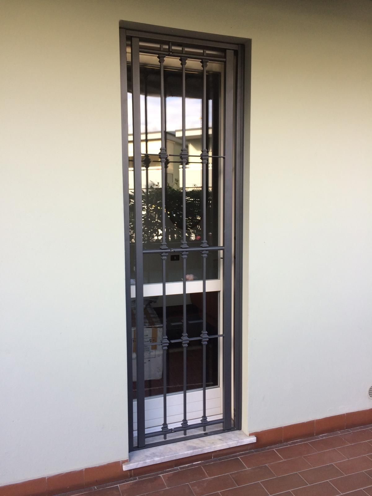 Una finestra alta e stretta con sbarre di sicurezza nere incastonate in un muro di colore chiaro, patio in mattoni rossi.