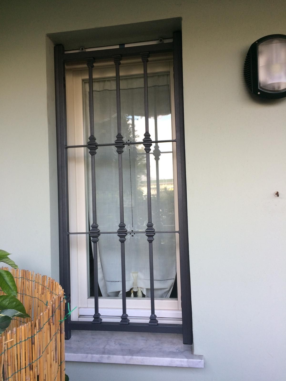 Finestra con sbarre di sicurezza nere su una parete verde chiaro, telaio della finestra bianco.