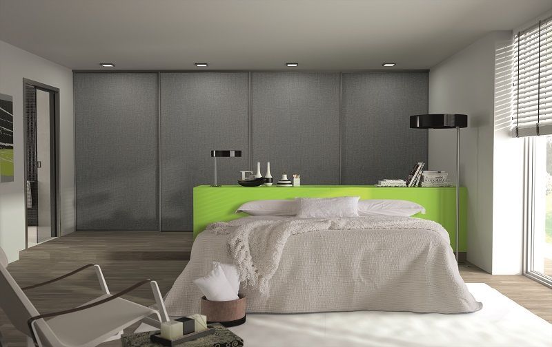 Camera da letto con parete decorativa verde, letto, ante dell'armadio grigie e finestra con persiane.