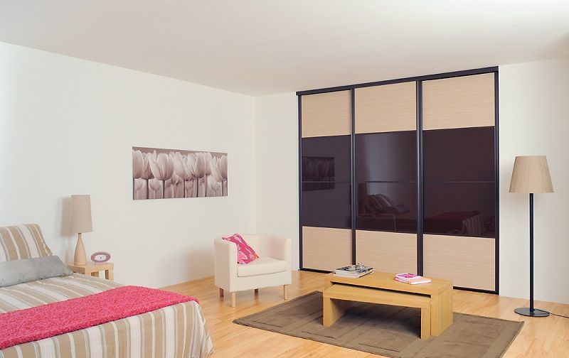 Interno della camera da letto con grande armadio con ante scorrevoli, pareti beige e pavimento in legno chiaro.