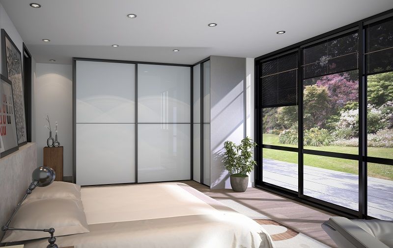 Camera da letto con ante scorrevoli, ampia finestra con tende, letto e pianta decorativa.