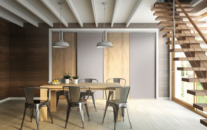 Sala da pranzo con tavolo in legno, sedie in metallo, lampade a sospensione e una scala.