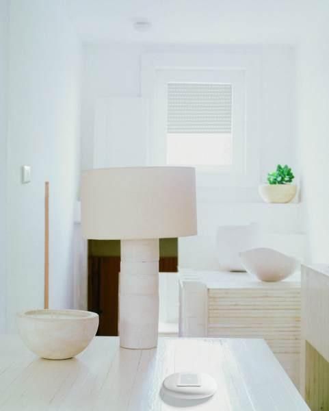 Interno bianco con tavolo, lampada e ciotole decorative; sullo sfondo c'è una finestra.