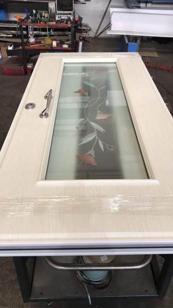 Porta beige con pannello in vetro smerigliato decorato con motivi floreali; appoggiata su un supporto in metallo.