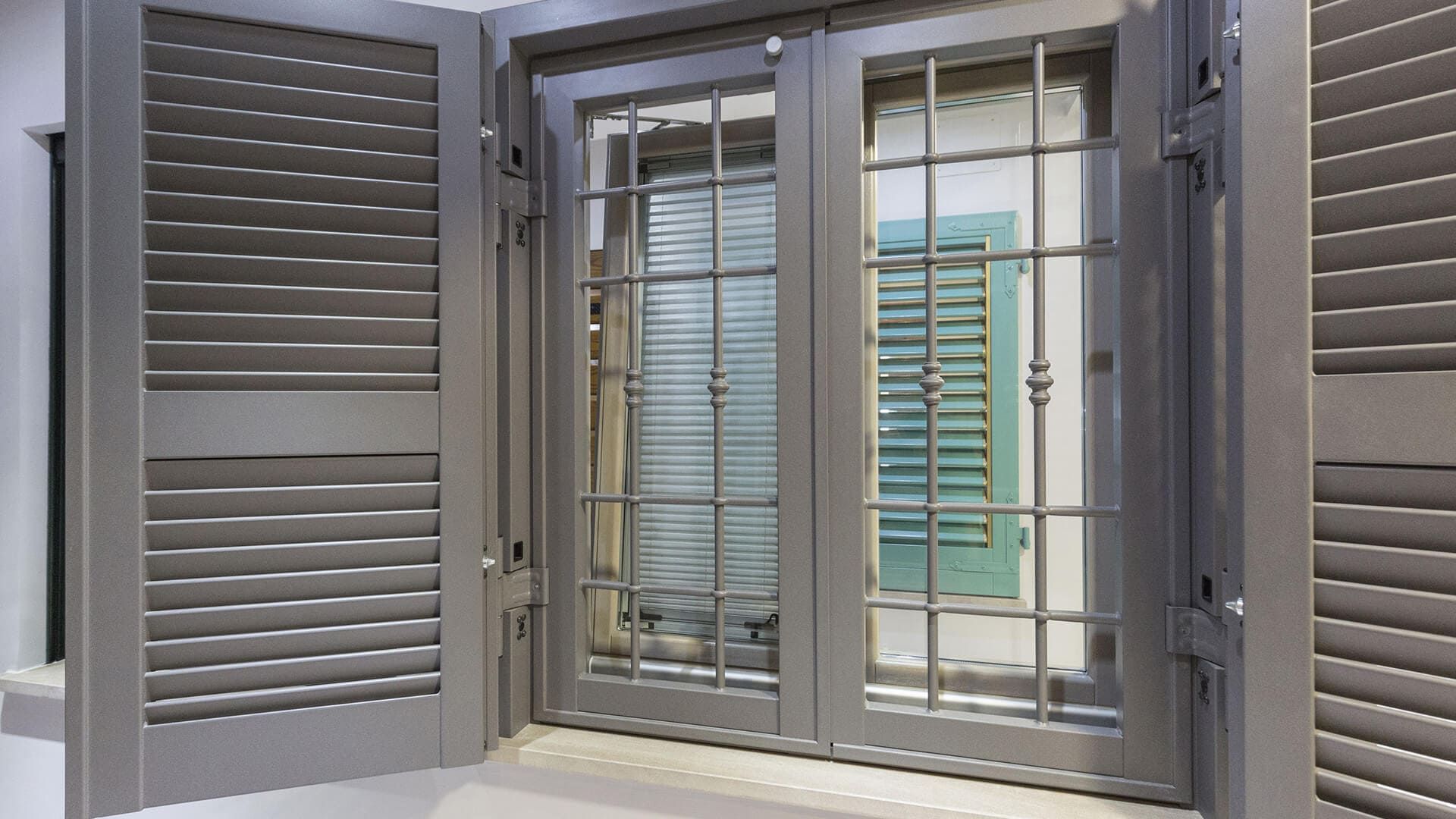 Finestra grigia con persiane, inferriate di sicurezza interne e persiana color verde acqua all'interno della finestra.