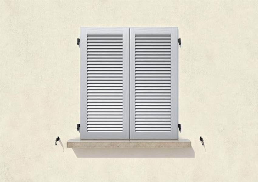 Persiane bianche con persiane su una finestra contro un muro chiaro con davanzale in pietra.