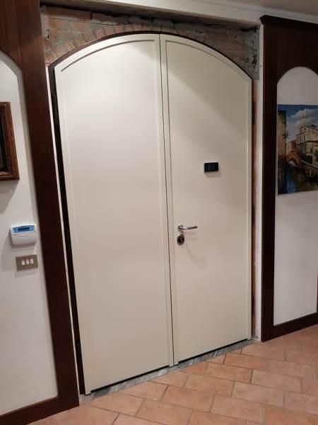 Doppie porte ad arco bianche con finiture in legno scuro, inserite in un interno in mattoni e piastrelle.