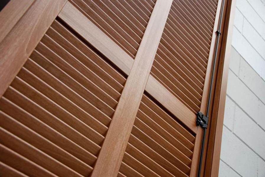 Pannelli porta in legno con persiane e supporti trasversali angolari. I pannelli sono marroni e si vede un chiavistello.