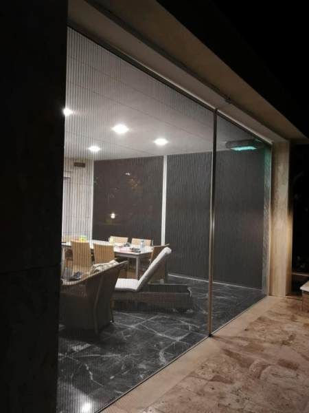 Sala da pranzo con pareti in vetro di notte; tavolo e sedie visibili, pavimento in marmo nero, patio esterno.