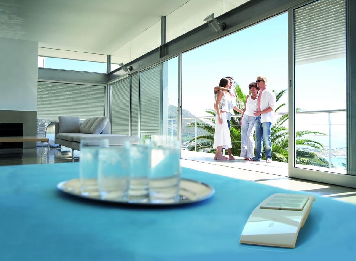 Famiglia su un balcone con vista sull'oceano, interno con divano blu, occhiali e telecomando.