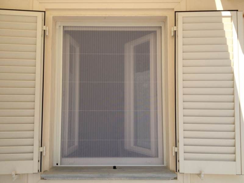 Finestra bianca con zanzariera e persiane aperte.
