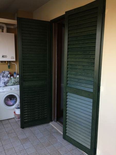 Le porte con persiane verdi si aprono su un patio piastrellato con lavatrice e scaldabagno.