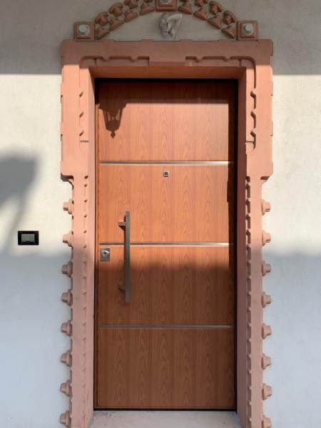 Porta in legno con cornice decorativa in pietra rosa e arco superiore decorato.