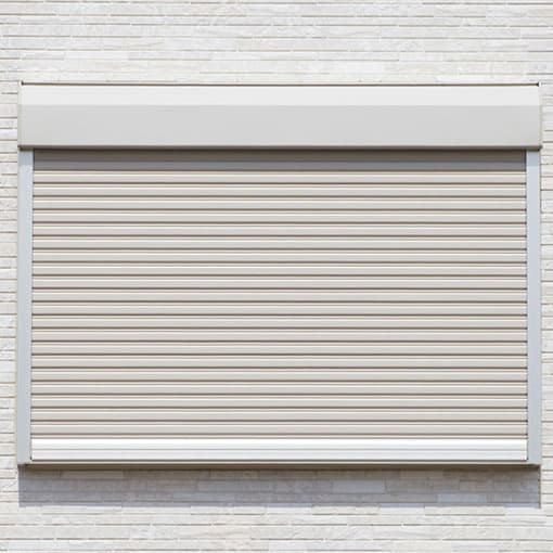 Tapparella marrone chiaro sopra una finestra su un muro di mattoni.