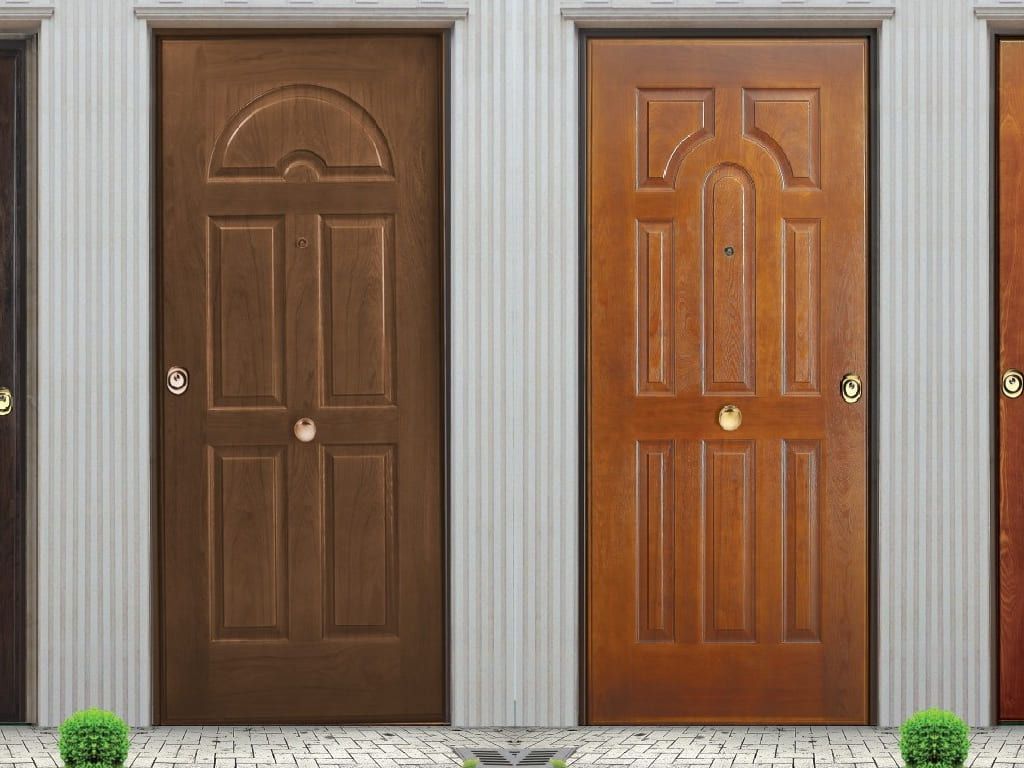 Due porte in legno con pannelli decorativi, tonalità marroni. Appoggiate a una parete strutturata, con piante sottostanti.